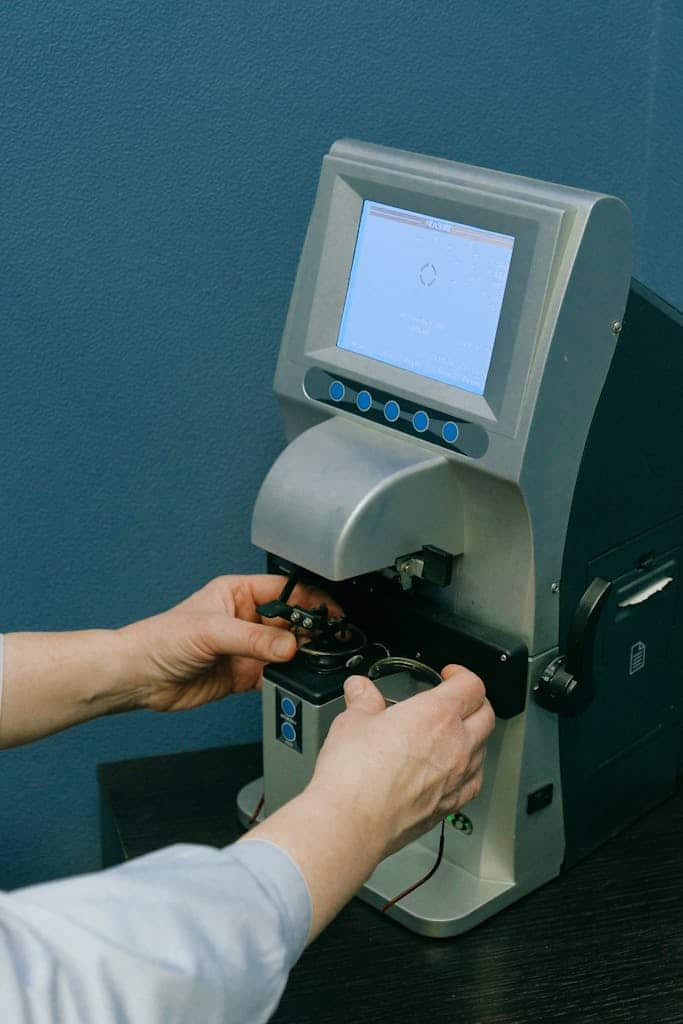 Crop anonymous medic in white wear adjusting automatic refkeratometer with small screen and blue buttons while working in doctor office